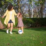 A mother and daughter enjoying a sunny day playing soccer in a lush green park.
